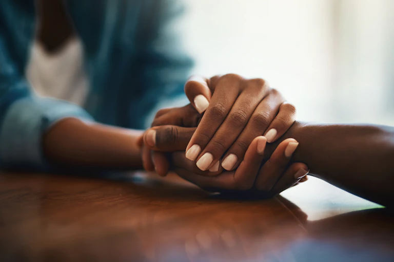 Close-up shot of two people holding hands in comfort.
