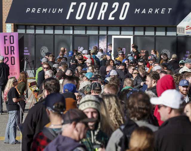 A crowd of people are seen outside a store called premium four20 market. 