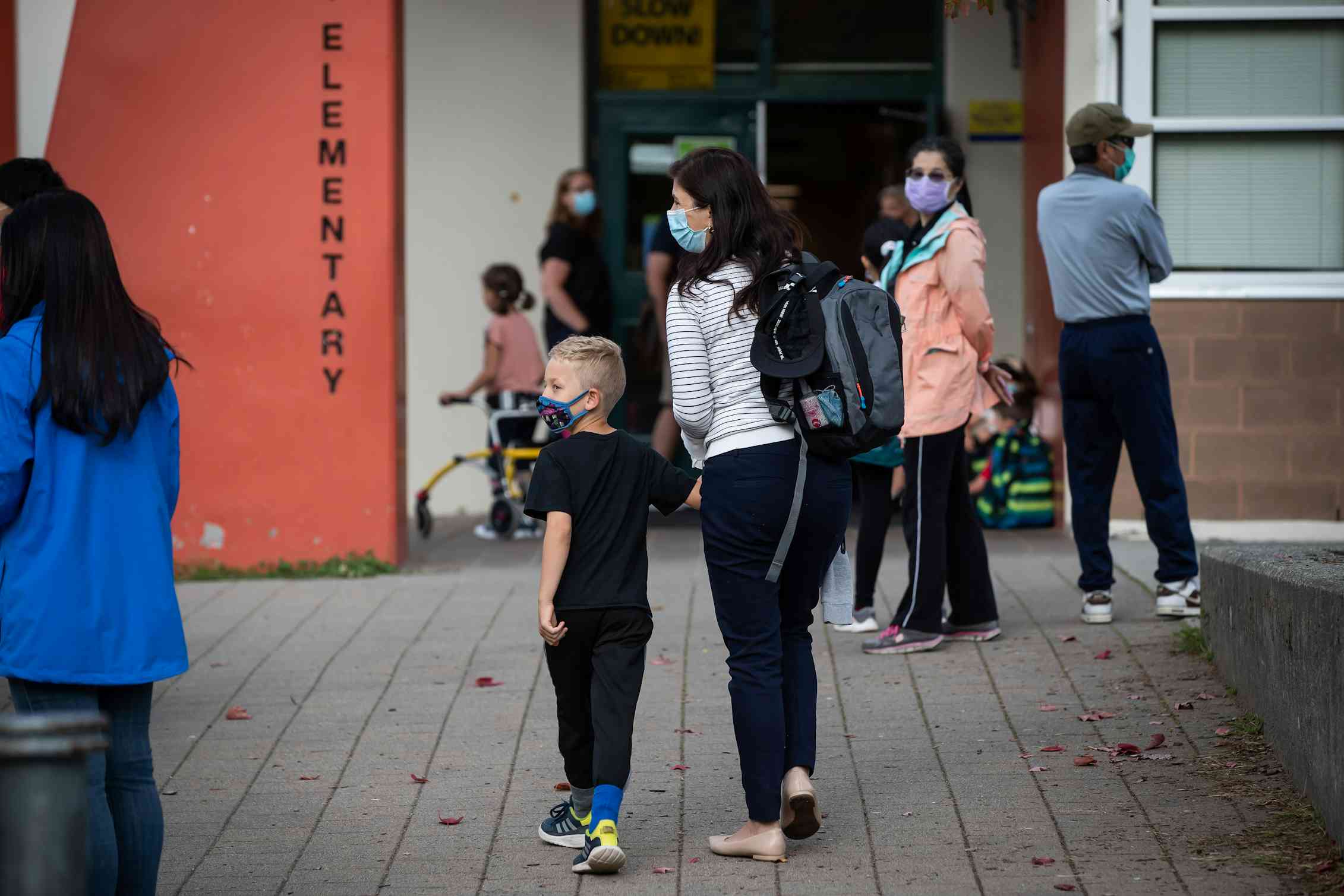 A parent and child in face mask arrive at a school yard