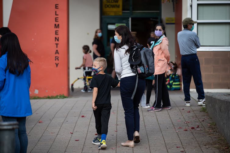 A parent and child in face masks arrive at a school yard