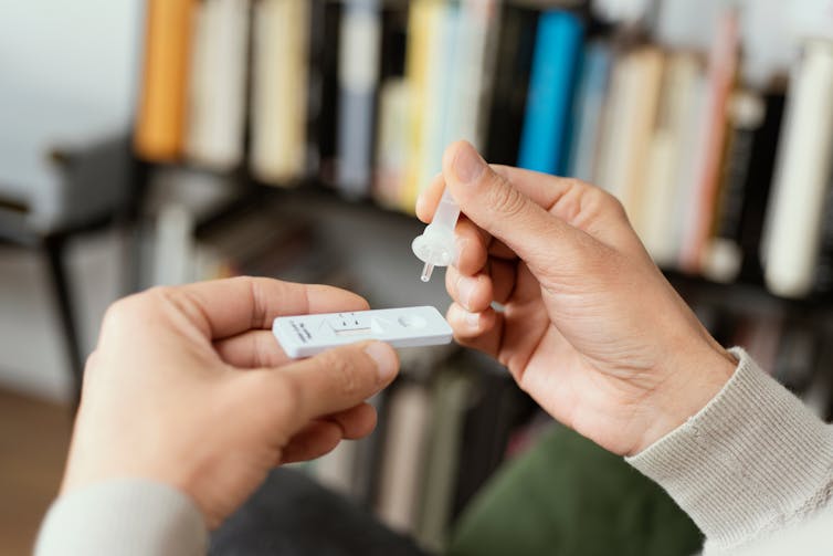 Person at home dropping reagent into a rapid antigen test