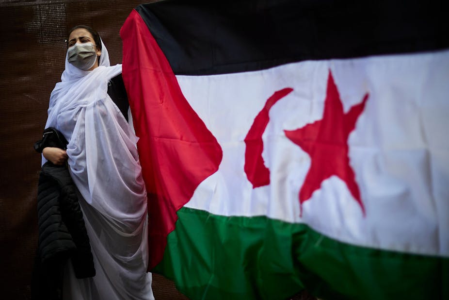 A woman dressed in Malahfa carries a big Sahara flag