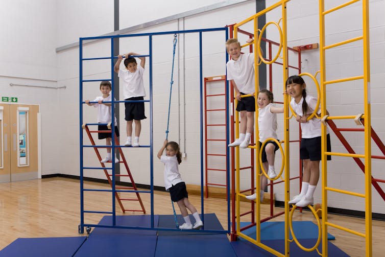 Primary school children climb on gymnastics equipment