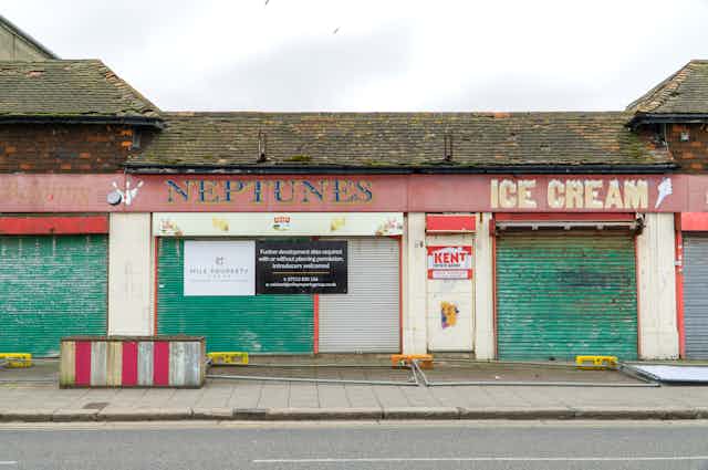 A row of dingy boarded-up shops painted red with green shutters.