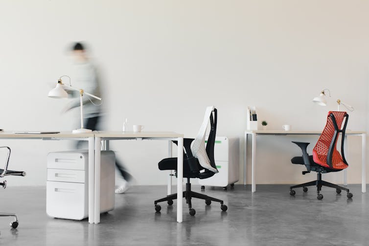 a person walks through a modern, minimalist office of chairs and desks.