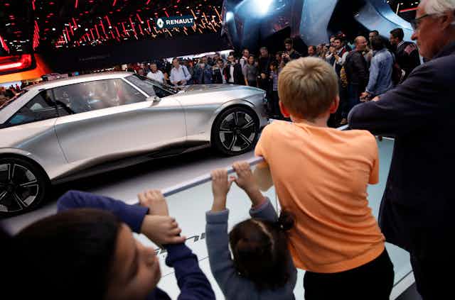 Kids and adults look towards a sleek silver car