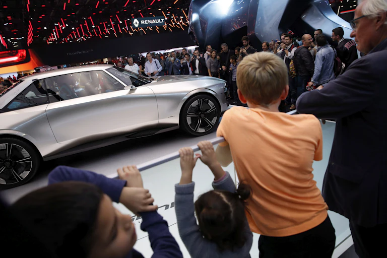 Kids and adults look towards a sleek silver car