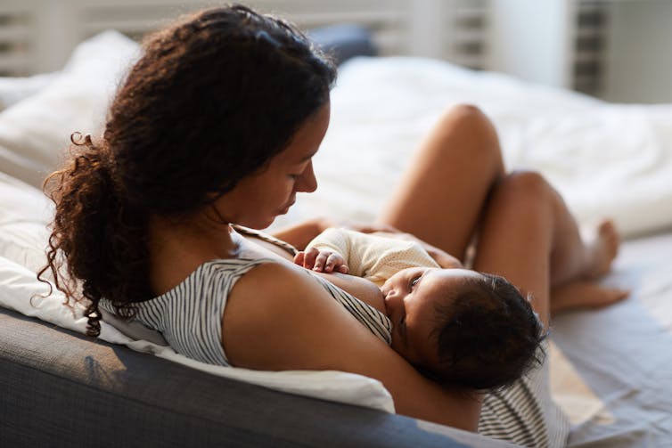 A woman breastfeeding a baby on a bed.