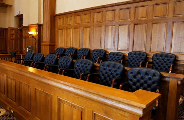 The black, upholstered seats of a 14-person jury box in a courtroom