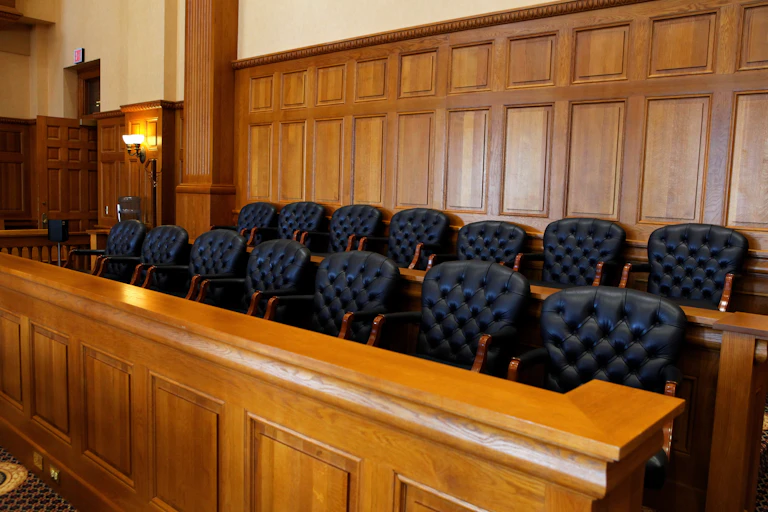 The black, upholstered seats of a 14-person jury box in a courtroom
