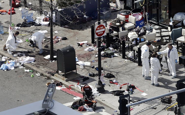Investigadores vestidos con trajes blancos examinando la escena del atentado en el maratón de Boston.