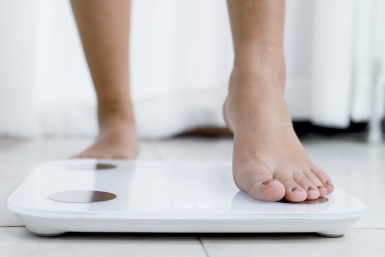 A person steps onto bathroom scales, their ankles and feet visible.