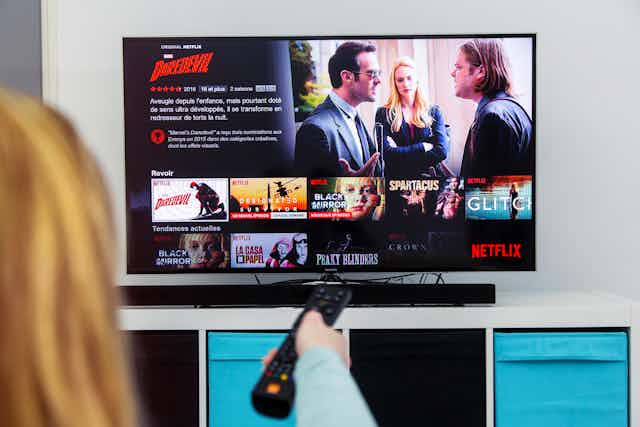 A woman points a remote control at a television with Netflix's homepage showing