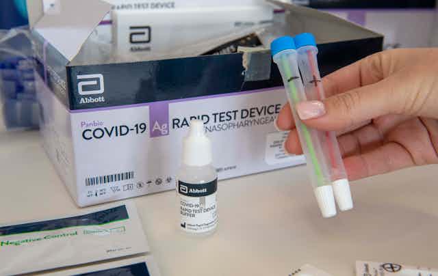 A manicured hand holds up a rapid test kit.
