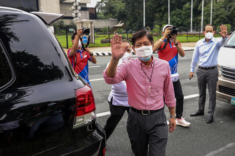 Ferdinand 'Bongbong' Marcos Jnr, raises his hand to salute supporters. In the background are press photographers.