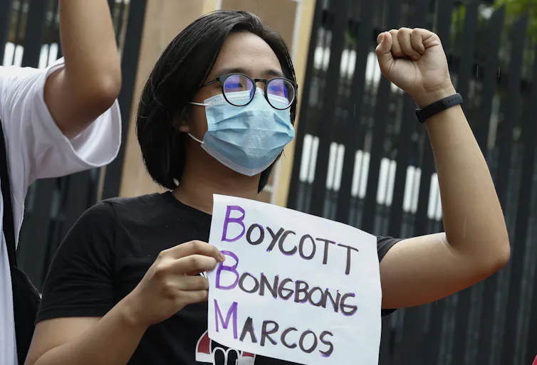 A woman carrying an anti-Marcos placard raises her fist in protest against 'Bongbong' Marcos's candidacy.