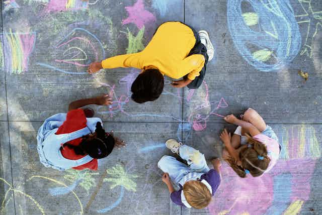 Four children draw on sidewalk with chalk