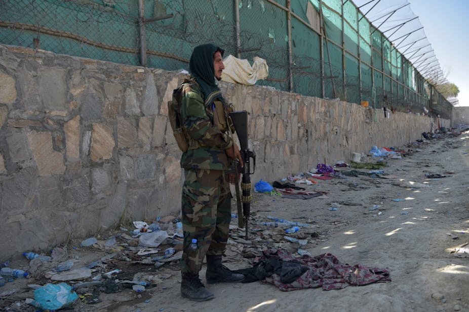 Un combattant taliban armé debout devant un mur au milieu de débris.