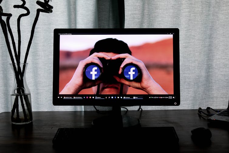 A desktop shows a man with binoculars that have the Facebook F on them.