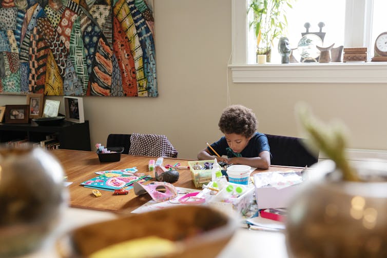 Boy draws at table partially covered with art supplies