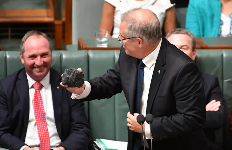 Man holds lump of coal and looks at other smiling man