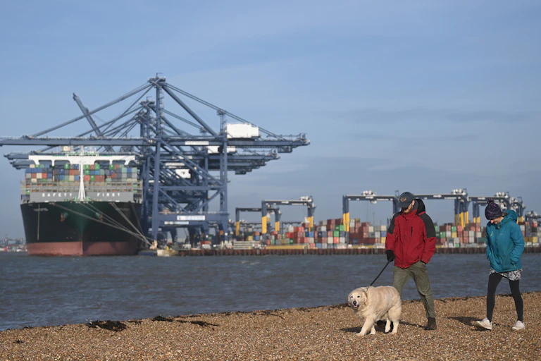 A container ship docking at Felixstowe as a couple walk on the beach