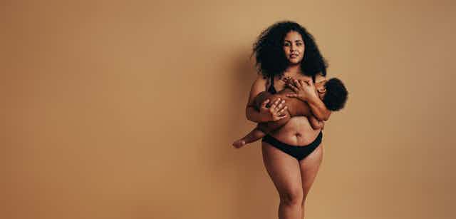 A young Black woman and new mother holding her baby in position to breastfeed.
