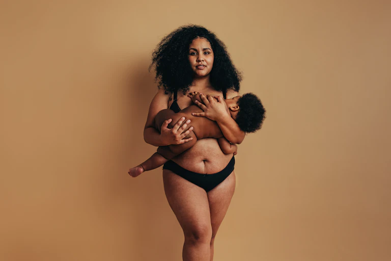 A young Black woman and new mother holding her baby in position to breastfeed.