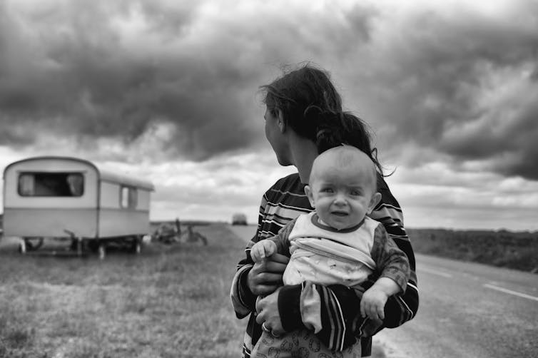 Woman with baby looking back at a caravan