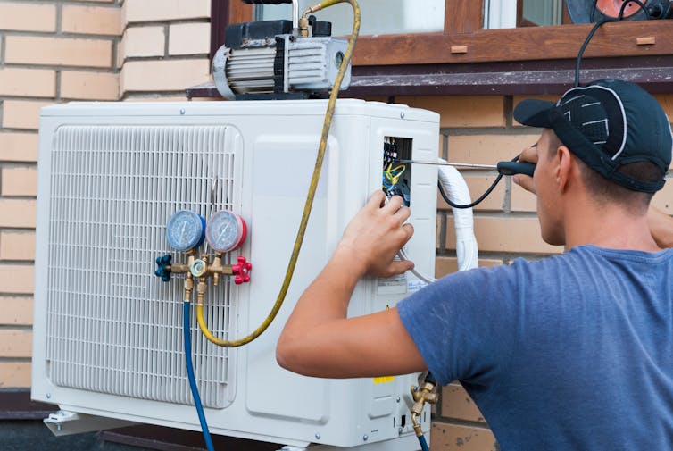 A worker uses a screwdriver on the fan unit of an air-source heat pump.