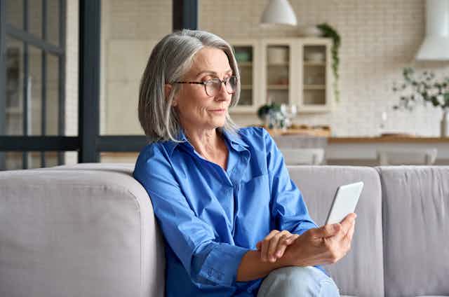 A middle-aged woman sitting on the couch looking at her smartphone.