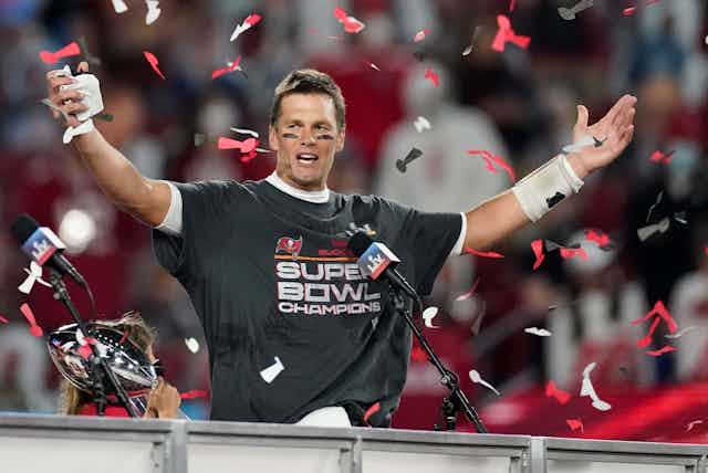 Tom Brady stands with his hands held out as confetti rains down on him