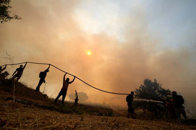People are silhouetted while holding up a fire hose