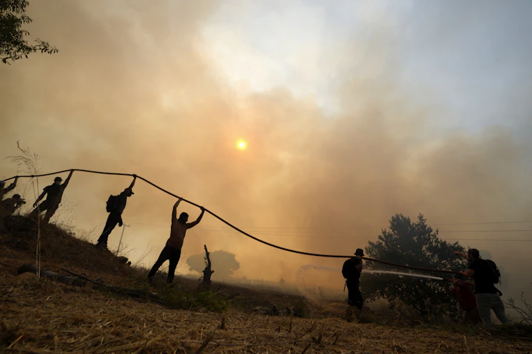 People are silhouetted while holding up a fire hose
