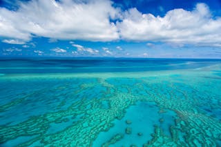 An aerial view of the an expansive reef with clouds in the sky.