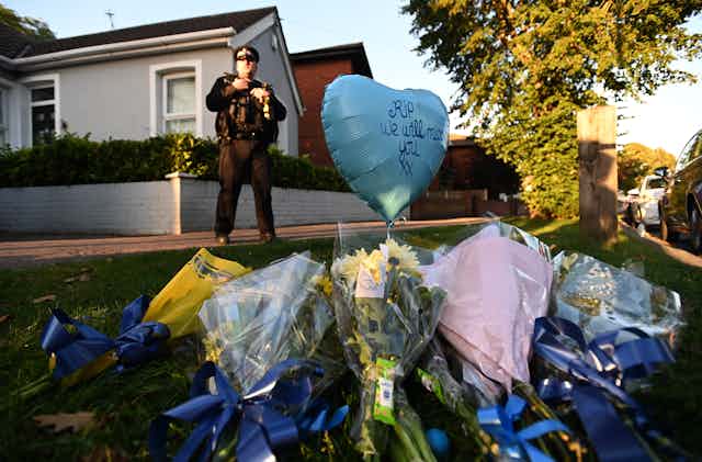 Flowers laid in Essex in memory of David Amess. A balloon reads 'RIP, we will miss you' and a police officer stands in the background.