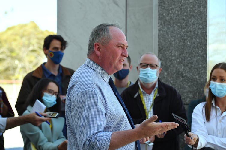 man in blue shirt talks to journalists