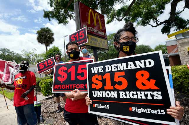 Workers protesting their wages carry signs in front of a McDonalds that say 'we demand $15 & union rights.'
