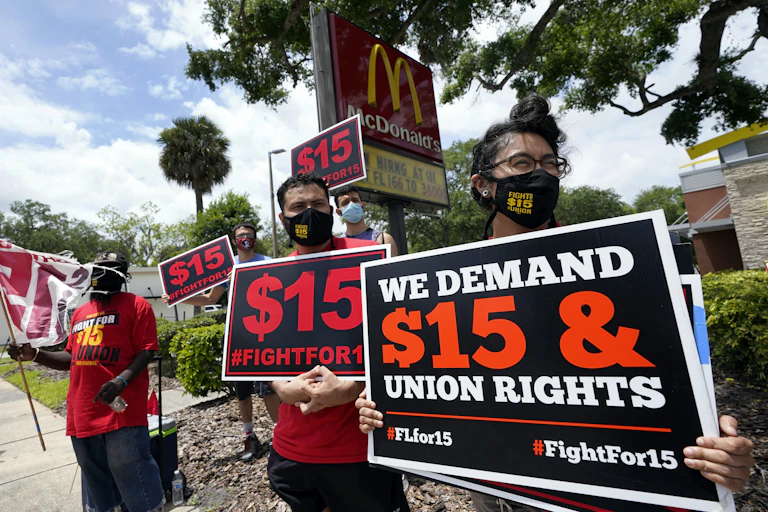Workers protesting their wages carry signs in front of a McDonalds that say 'we demand $15 & union rights.'