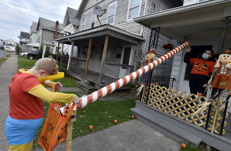 A woman wearing a face mask sends candies down a chute to a boy trick-or-treating