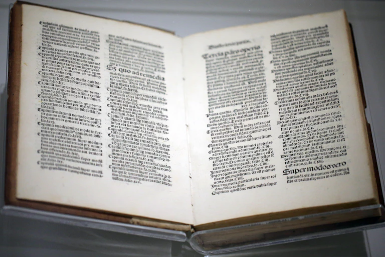 A museum case displays open pages from a medieval manuscript about witches.