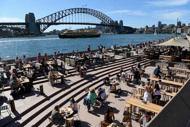 People dining outdoors in front of the Sydney Harbour Bridge
