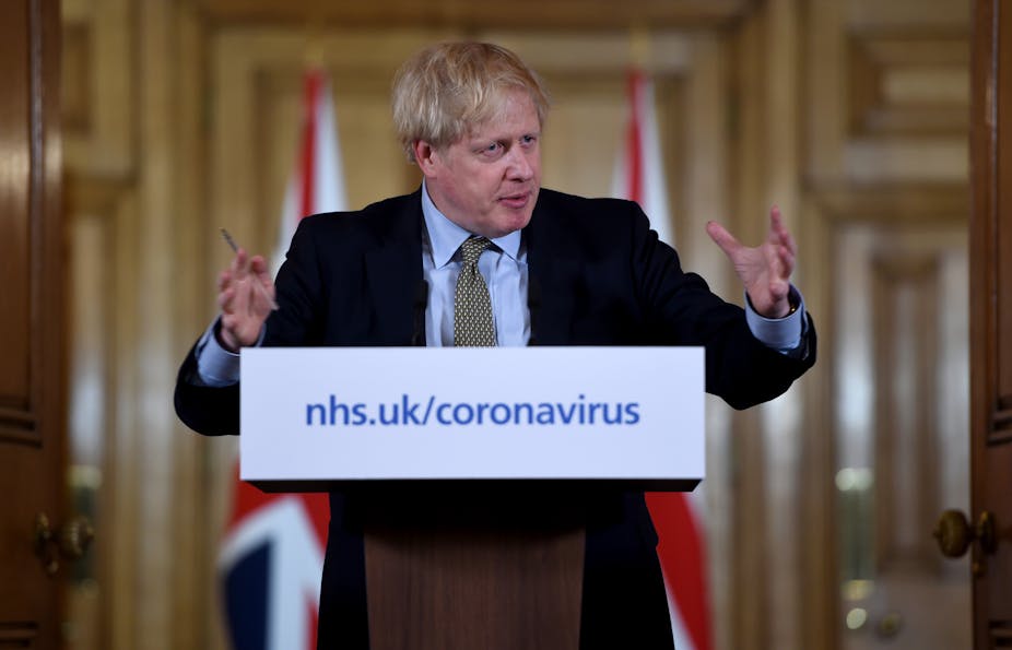 Prime Minister Boris Johnson gestures during a press conference behind a podium with placard reading nhs.uk/coronavirus
