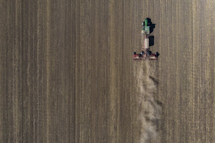 A green tractor pulls a seed drill behind it on a ploughed field.