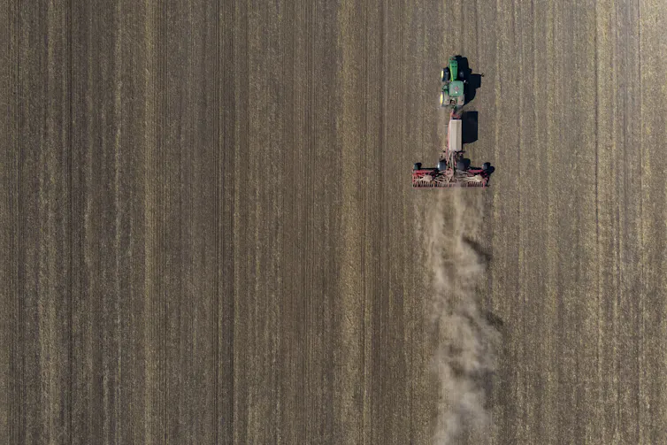 A green tractor pulls a seed drill behind it on a ploughed field.