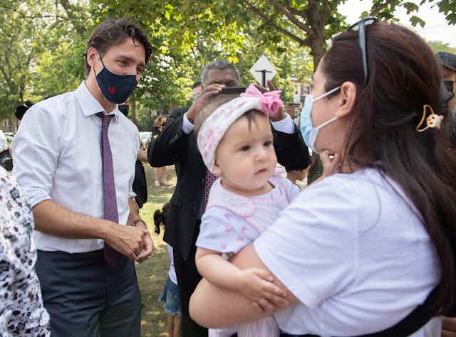Justin Trudeau, wearing a mask, talks to a mother and her baby. The mother is also masked.