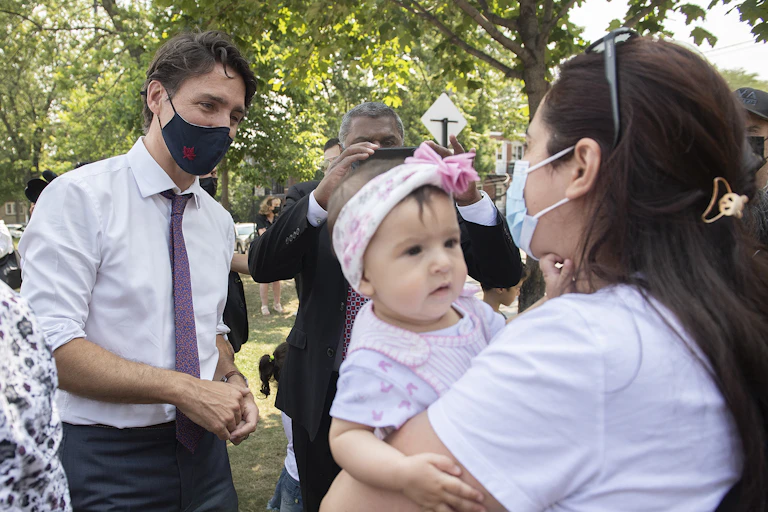 Justin Trudeau, wearing a mask, talks to a mother and her baby. The mother is also masked.