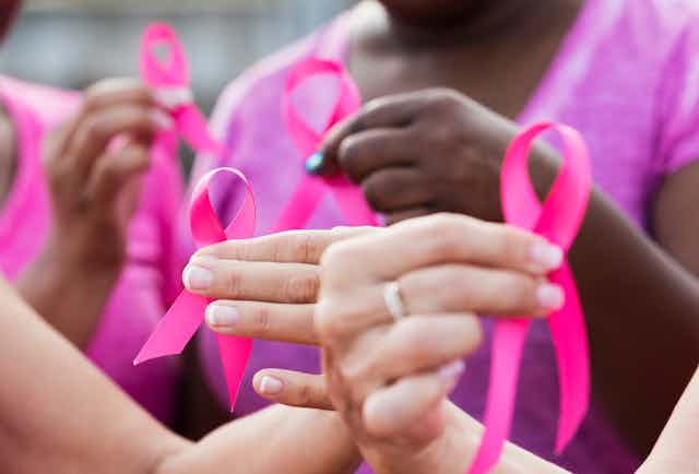 four multi-ethnic women wearing pink shirts, holding breast cancer awareness ribbons. The focus is on one of the hands.
