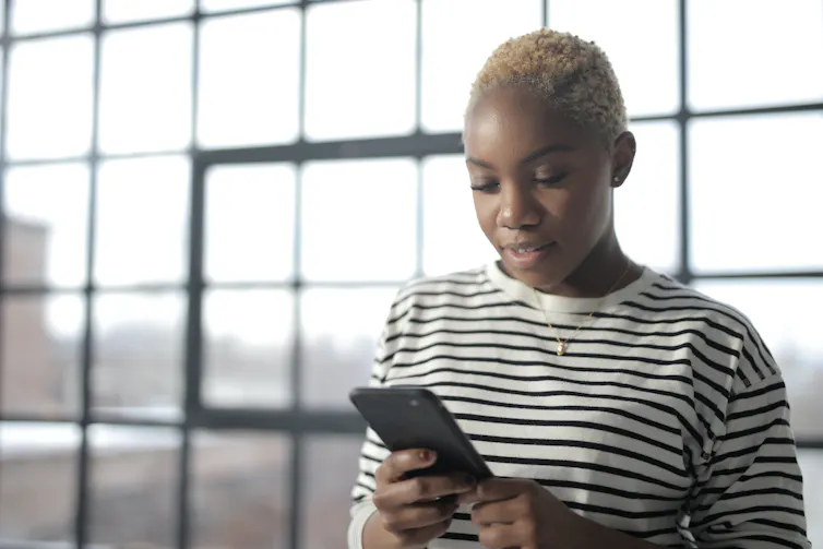 A woman in a striped shirt looks down at her phone.