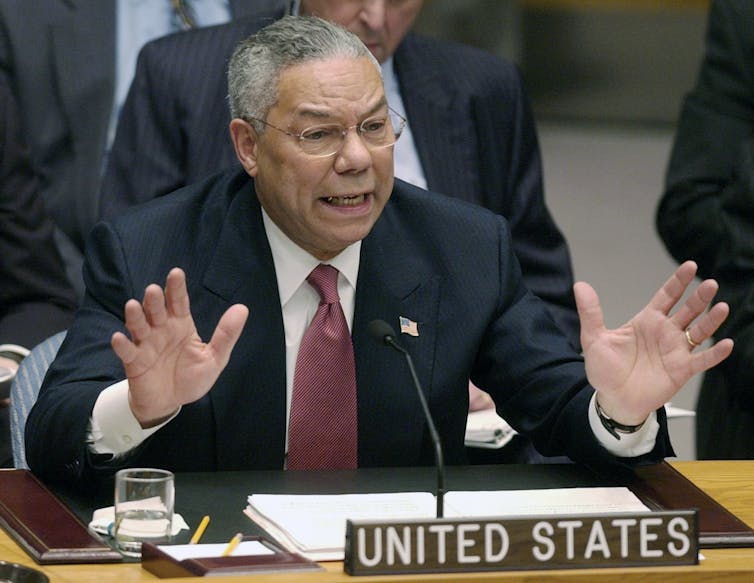 Colin Powell, sentado atrás de um microfone e na placa de identificação dos 'Estados Unidos', fala ao Conselho de Segurança das Nações Unidas.
